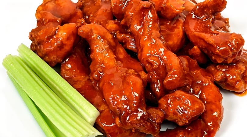 Close-up of boneless buffalo wings coated in glossy red sauce, served with fresh celery sticks.