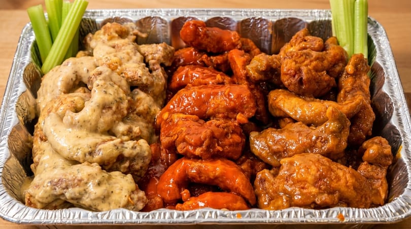 A foil tray filled with three sections of chicken wings: creamy garlic, spicy red, and BBQ.