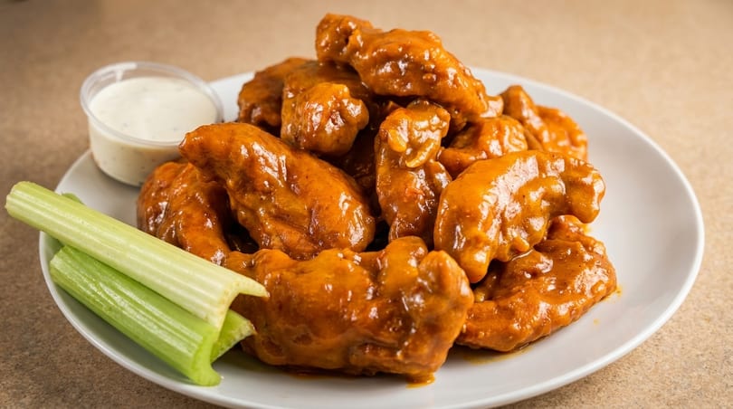 Plate of buffalo wings with celery sticks and a side of ranch dressing.